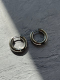 Two silver-toned metal hoop earrings with a split-ring design, resting on a textured gray surface under direct sunlight.