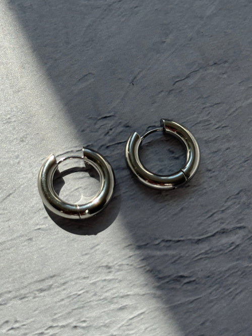 Two silver-toned metal hoop earrings with a split-ring design, resting on a textured gray surface under direct sunlight.