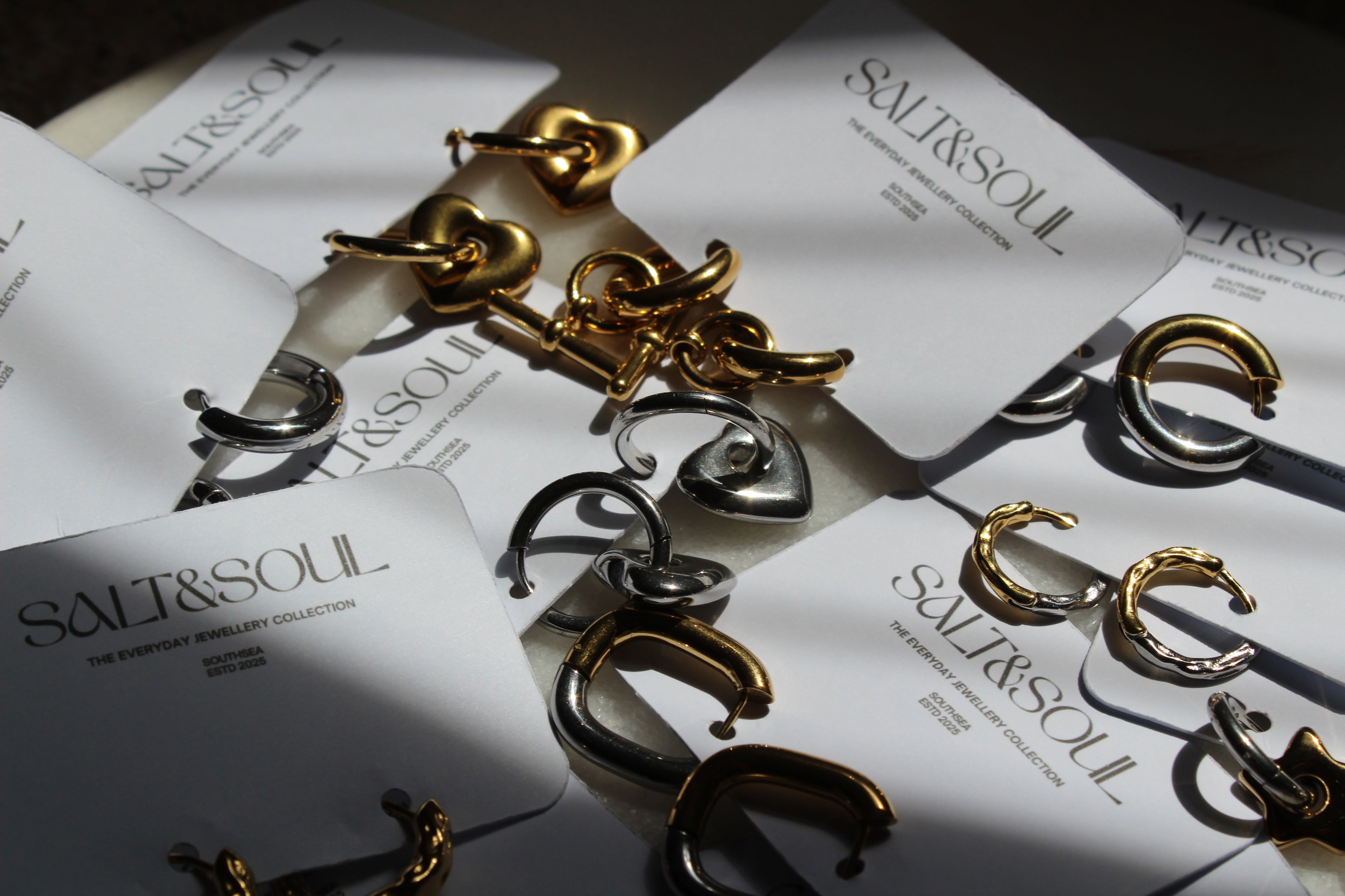 Gold and silver C-shaped hoop earrings displayed on white cards printed with the brand name 'SALT&SOUL'.