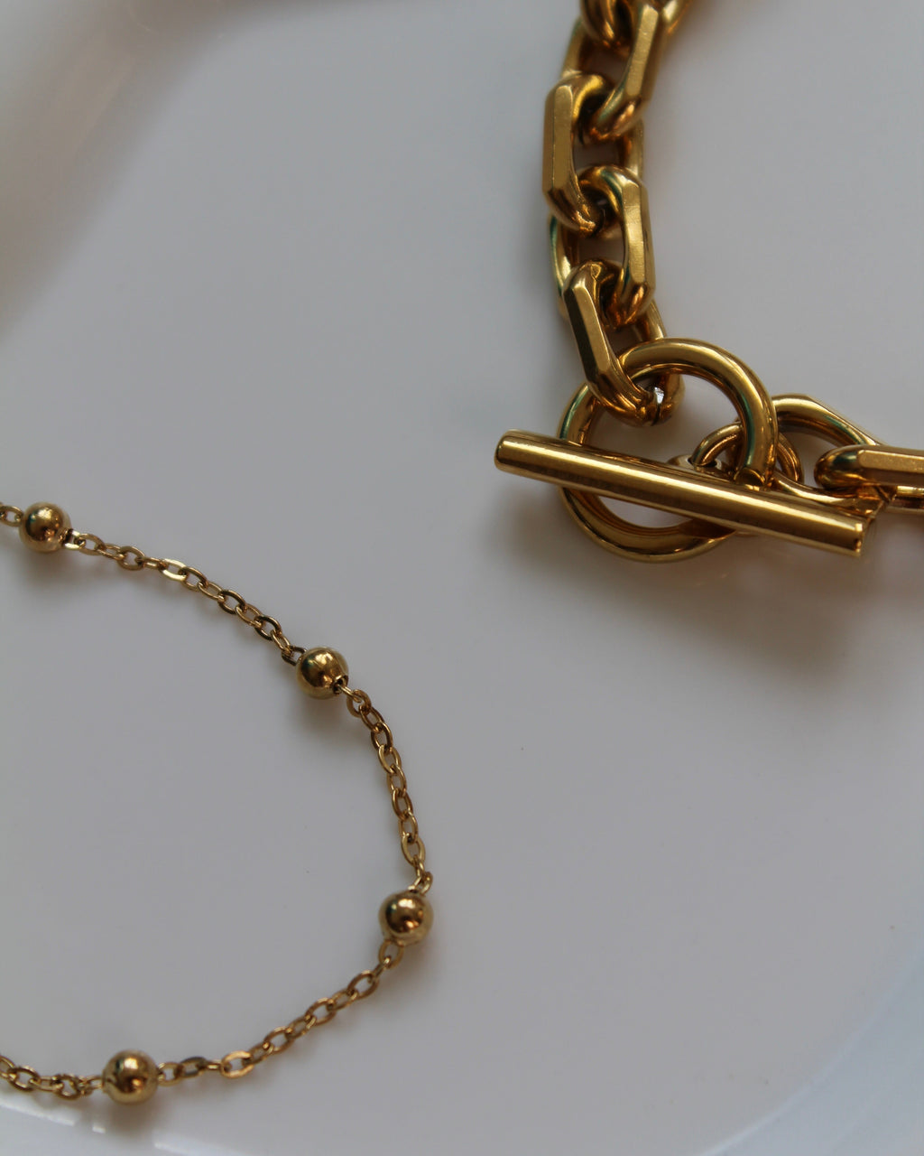 Gold-tone jewelry set featuring a chunky chain link bracelet with a toggle clasp and a delicate beaded chain bracelet, displayed on a clean white surface.