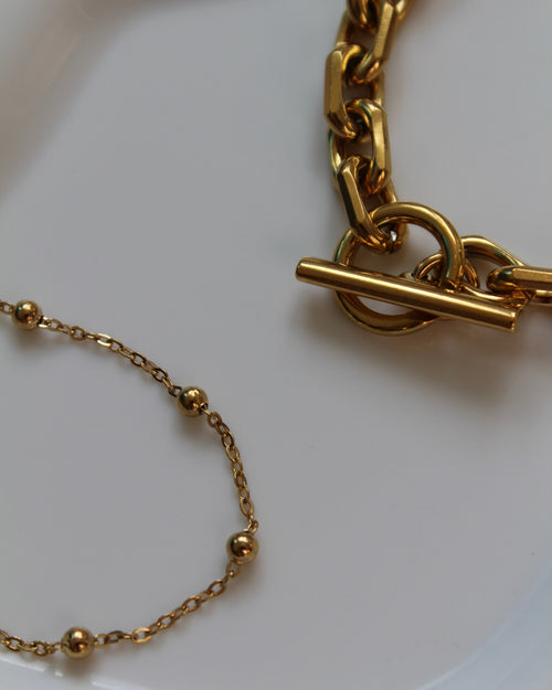Gold-tone jewelry set featuring a chunky chain link bracelet with a toggle clasp and a delicate beaded chain bracelet, displayed on a clean white surface.