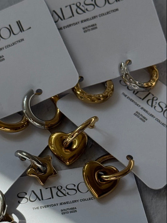 A styled flat-lay of gold and silver hoop earrings on white display cards printed with the brand name 'SALT&SOUL'.