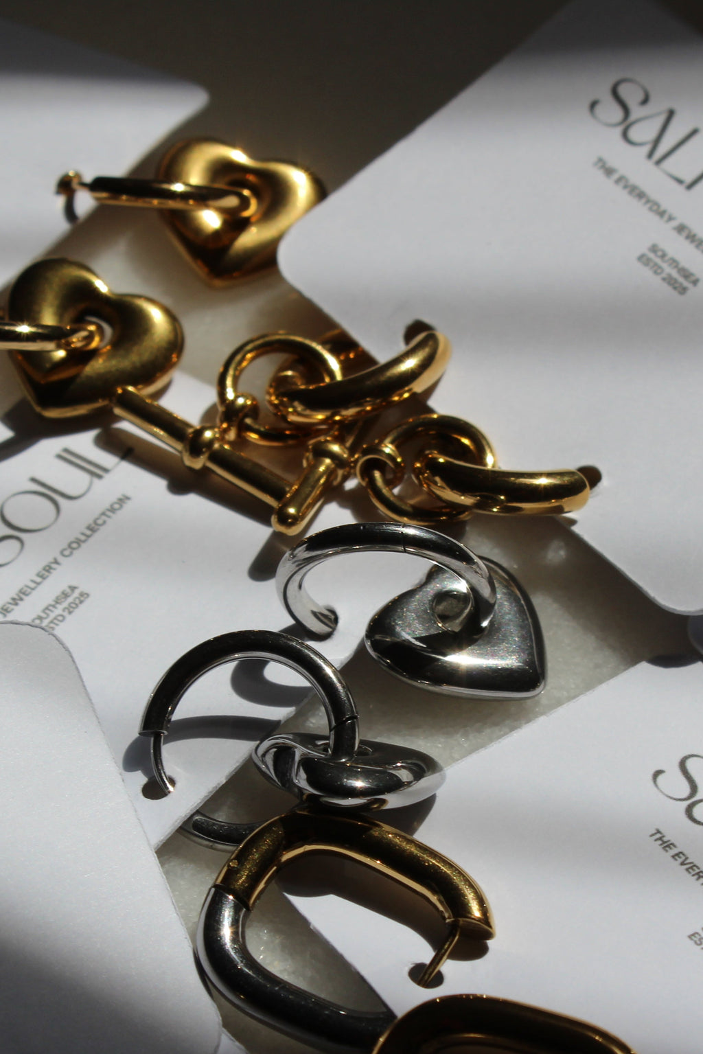Gold and silver C-shaped hoop earrings displayed on white cards printed with the brand name 'SALT&SOUL'.
