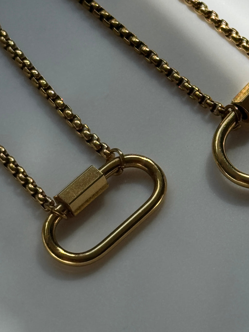 Gold-toned metal chain necklace with a large open oval ring pendant and a small rectangular clasp, shown on a light gray background.