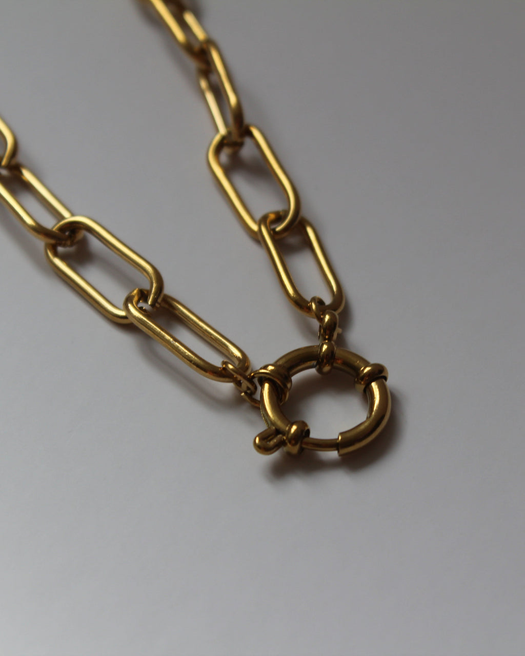 A gold-toned chain necklace with elongated paperclip-style links and a small interlocking ring clasp, photographed on a plain light background.