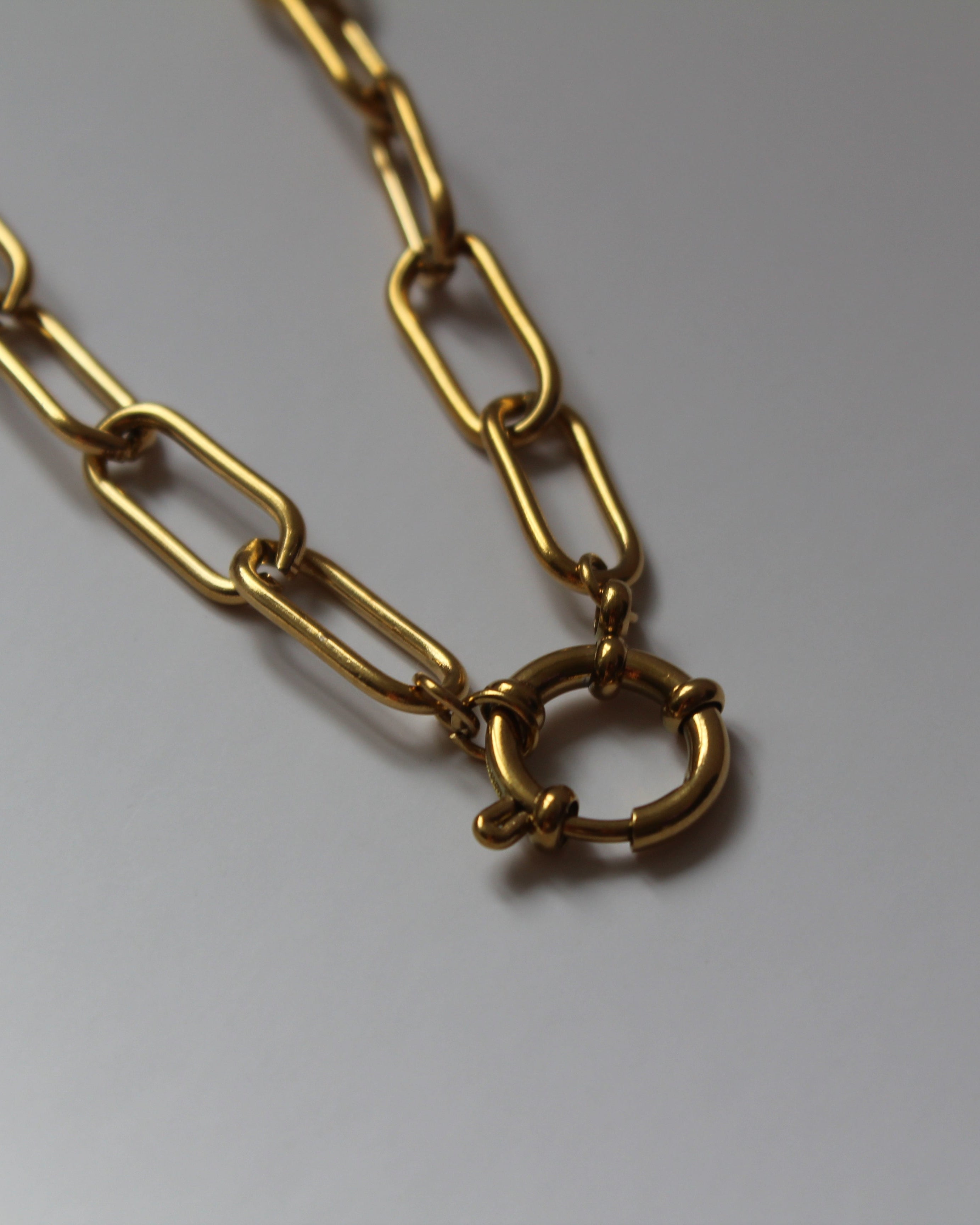 A gold-toned chain necklace with elongated paperclip-style links and a small interlocking ring clasp, photographed on a plain light background.